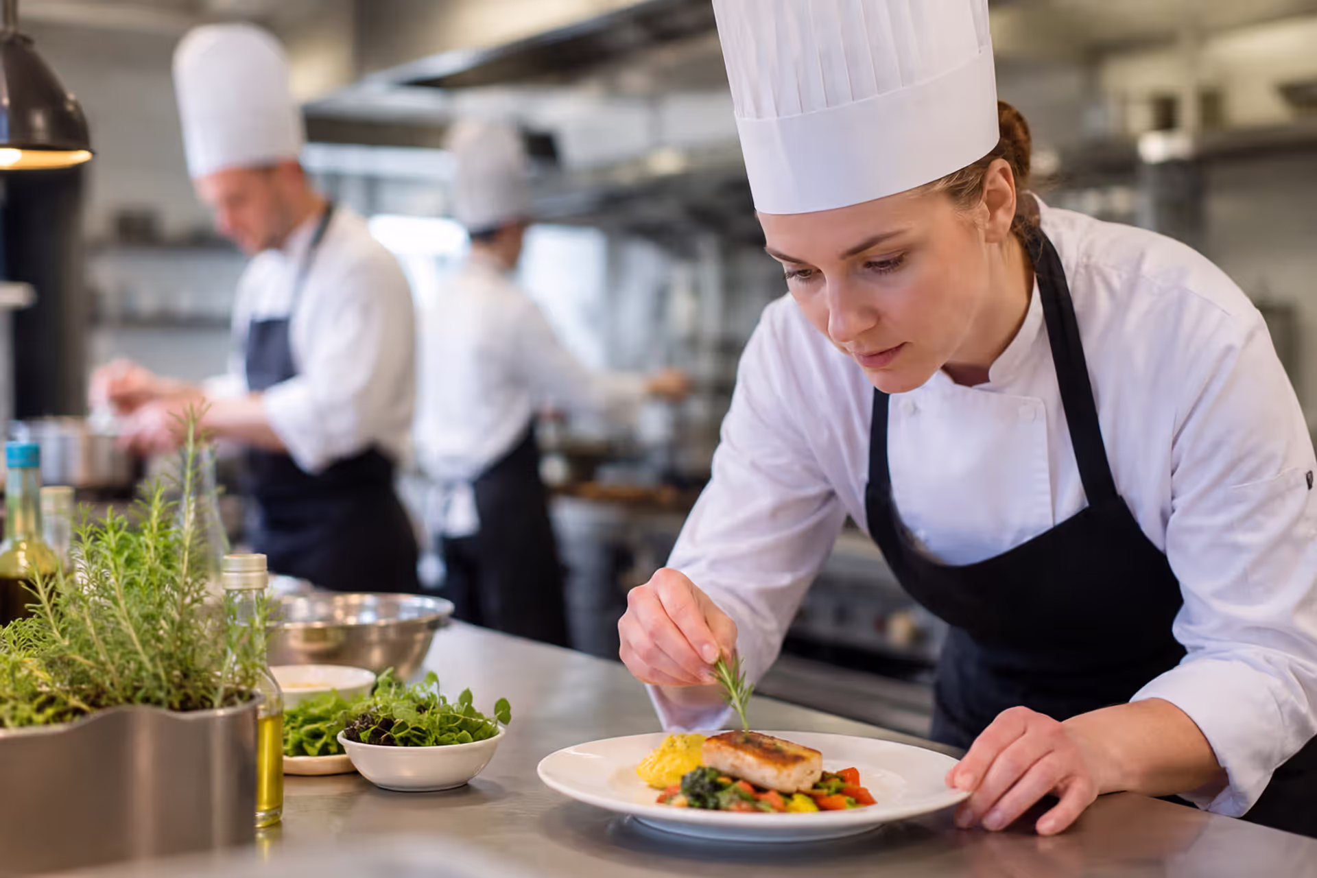Professional culinary arts student plating gourmet dish in commercial kitchen